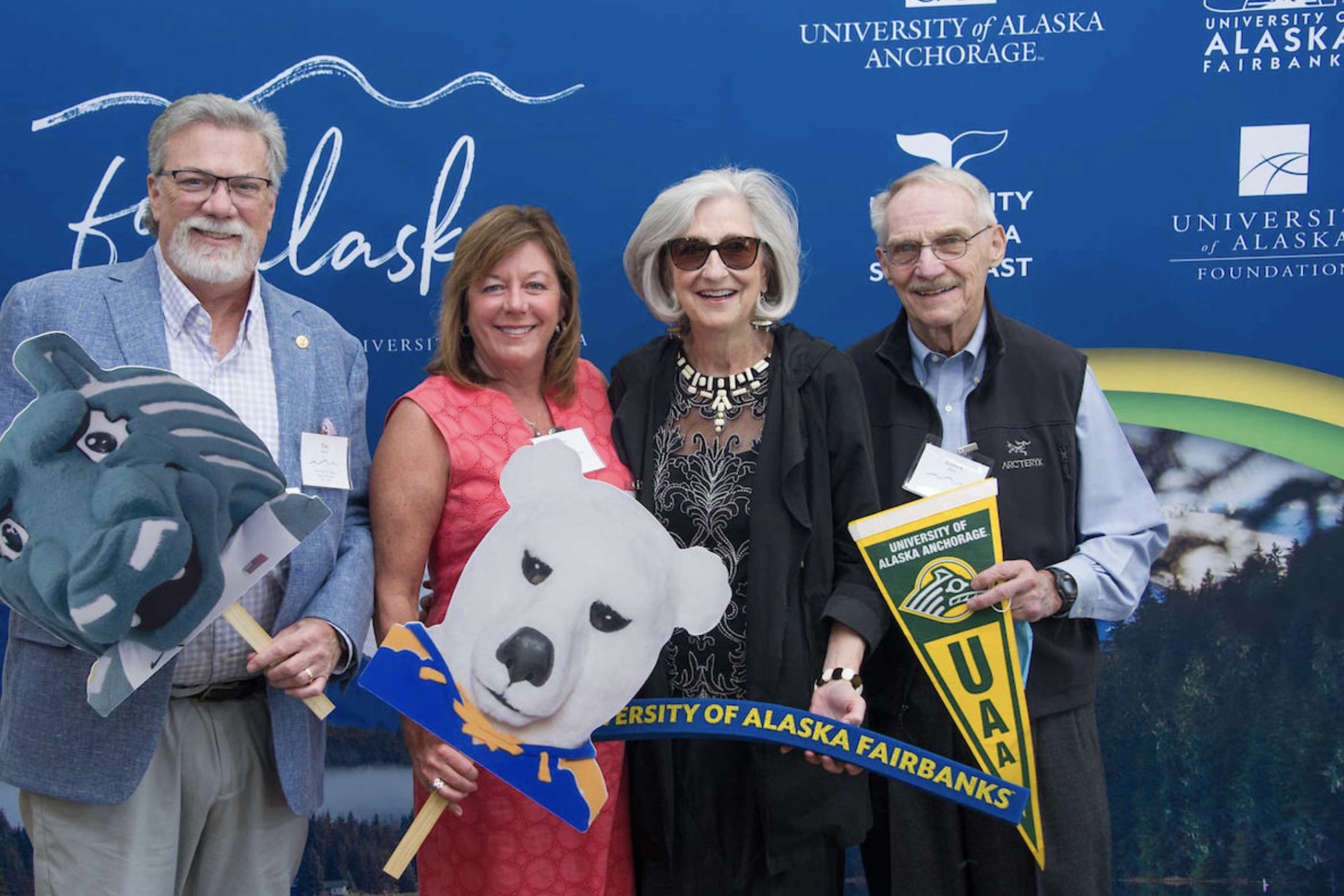 (From left to right) Tim Brady (BOR 2005 - 2015) and Betty Brady, with Mary K. Hughes (BOR 2002 - 2025; BOD 1989 - current) and Andrew Eker in front of a blue UA Foundation backdrop. 