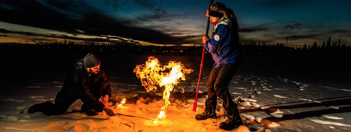 Two researchers set fire to methane gas released from a lake at dusk