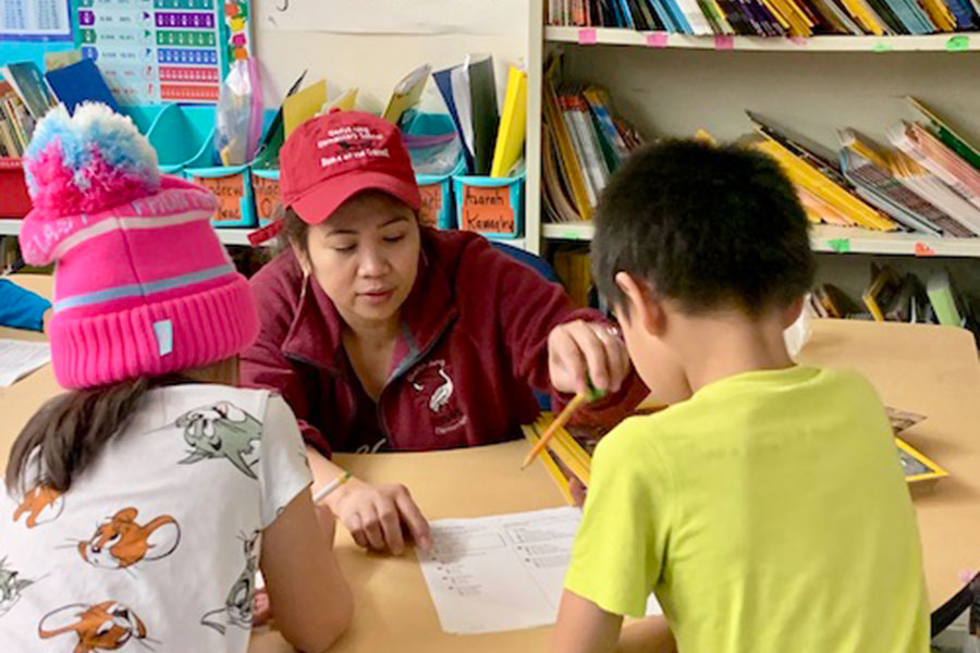 A teacher seated at a table with children instructing them on a group activity