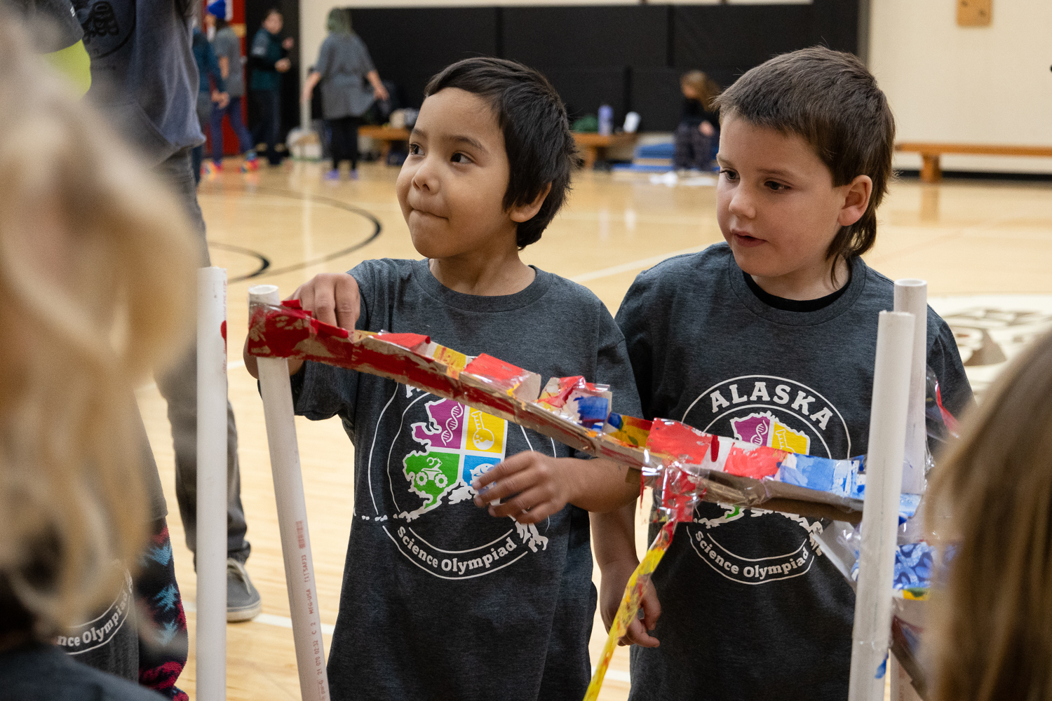 A student prepares to drop a marble in their roller coaster design made of painted pieces of cardboard, packaging tape, and sections of PVC pipe.