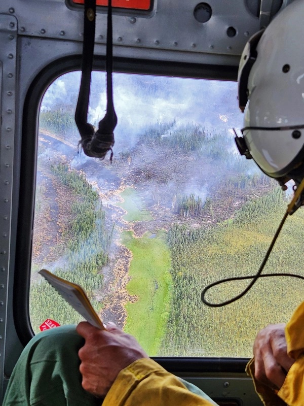 A firefighter looks down on the 2023 McCoy Creek fire from a helicopter. 