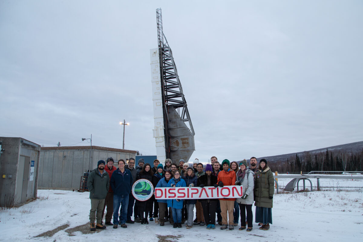 The Dissipation team poses in front of the vertical rocket with the mission logo