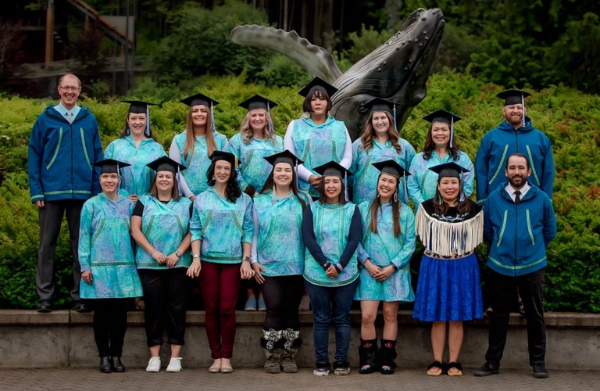 14 graduates stand with several faculty members 