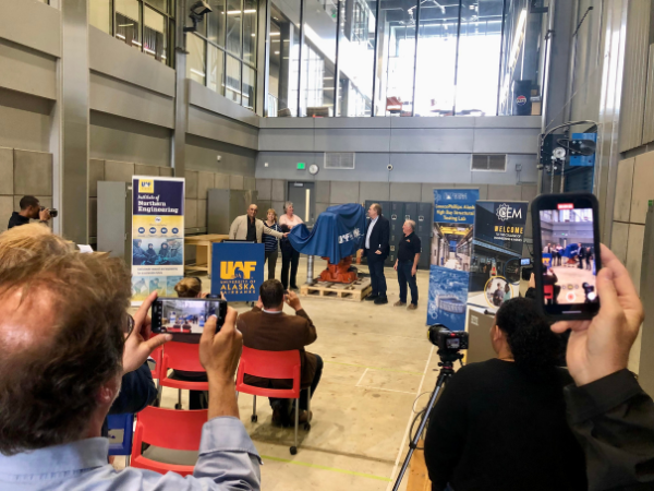 Leaders pull a blue sheet off the 3D robotic arm inside UAF's engineering building. 