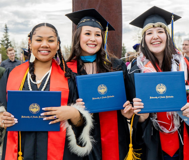 three UAF grads hold up diplomas