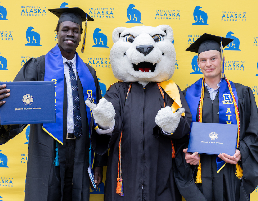 two student athlete grads pose with the UAF mascot after walking the stage