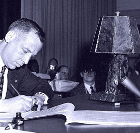 Delegate George Cooper signs the Alaska Constitution. The lamp made from jade collected by Marvin Marston sits behind him on the table.